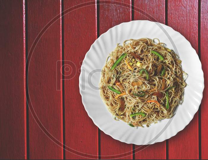 Vegetarian Schezwan Noodles Or Vegetable Hakka Noodles Or Chow Mein In White Plate At Wooden Background. Schezwan Noodles Is Indo-Chinese Cuisine Hot Dish With Udon Noodles, Vegetables And Chilli Sauce
