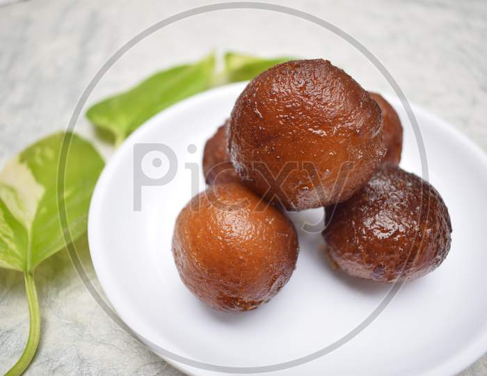 Close Up Of Gulab Jamun Sweet Indian Dessert On White Background On White Plate. Decorated With Moneyplant Leaves.