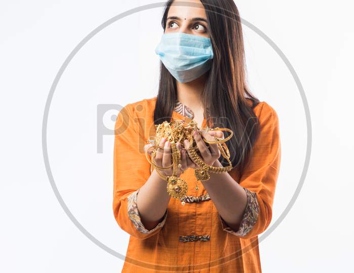 Indian Young Woman Wearing Face Mask And Holding Gold Jewelry Or Ornaments In Hand