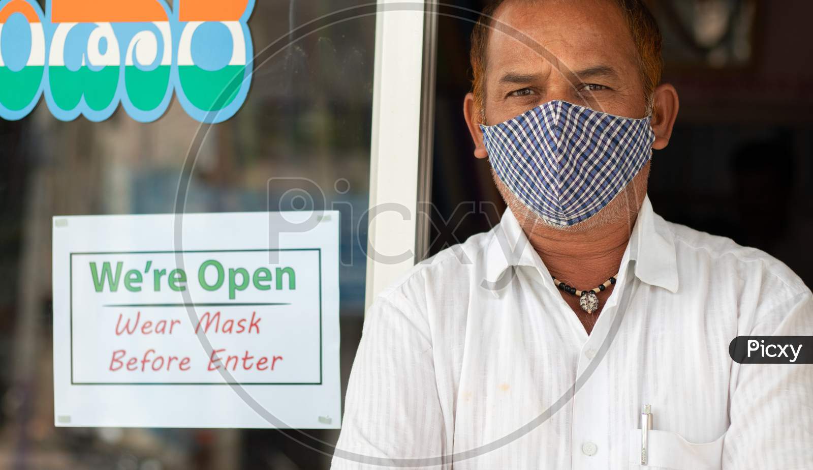 Small Business Owner In Medical Mask Standing In Front Of Door With We Are Opn Wear Mask Notice Board - Concept Of Support Local Community During Coronavirus Or Covid-19.