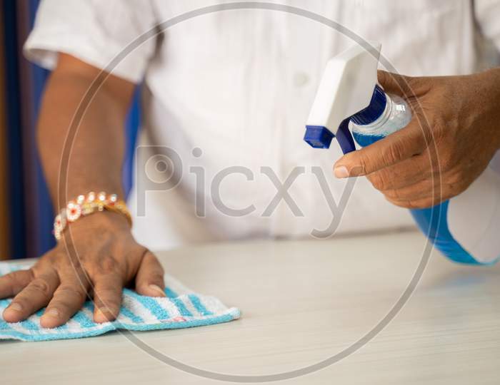Close Up Of Hands Disinfecting Table By Using Sanitizer - Cleaning Dust On Desk Surface With Cloth And Disinfectant Spray, To Protect From Coronavirus Or Covid-19 Infection.