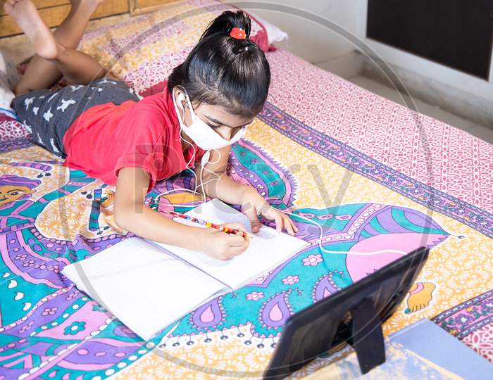 Little Girl Kid Student Wearing Mask Studying With Tablet At Home, Distance Learning Online Education.Covid-19 Coronavirus.Social Distancing, Home Schooling.