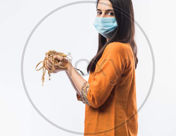 Indian Young Woman Wearing Face Mask And Holding Gold Jewelry Or Ornaments In Hand