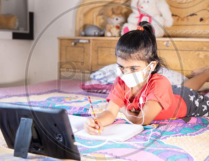 Little Girl Kid Student Wearing Mask Studying Online Class With Tablet At Home, New Normal.Covid-19 Coronavirus.Social Distancing, Home Schooling.