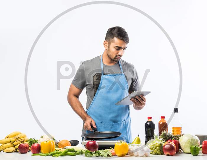 Handsome Indian Man In Kitchen Cooking Food While Wearing Appron