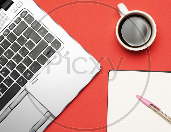 Work Space With Laptop Note Book Ball Pen And Coffee On Red Background. Flat Lay.