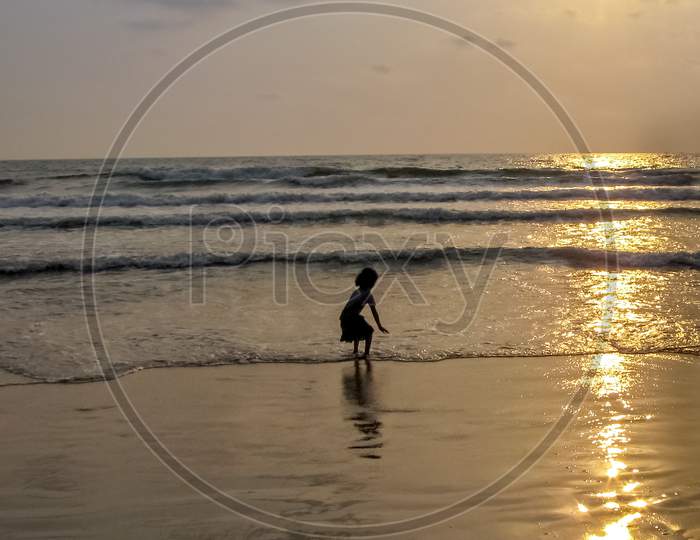 Sillhoutte Image Of A Young Girl Playing In Sea On A Background Of Nice Sunset.