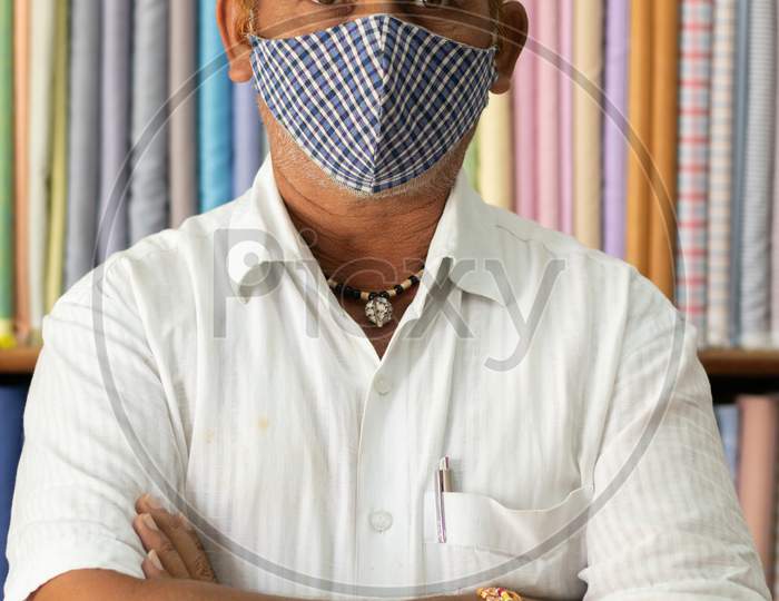 Portrait Of Shopkeeper Looking At Camera In Cloth Store Wearing Protective Medical Mask To Prevent Coronavirus Or Covid-19 And Standing With Arms Crossed