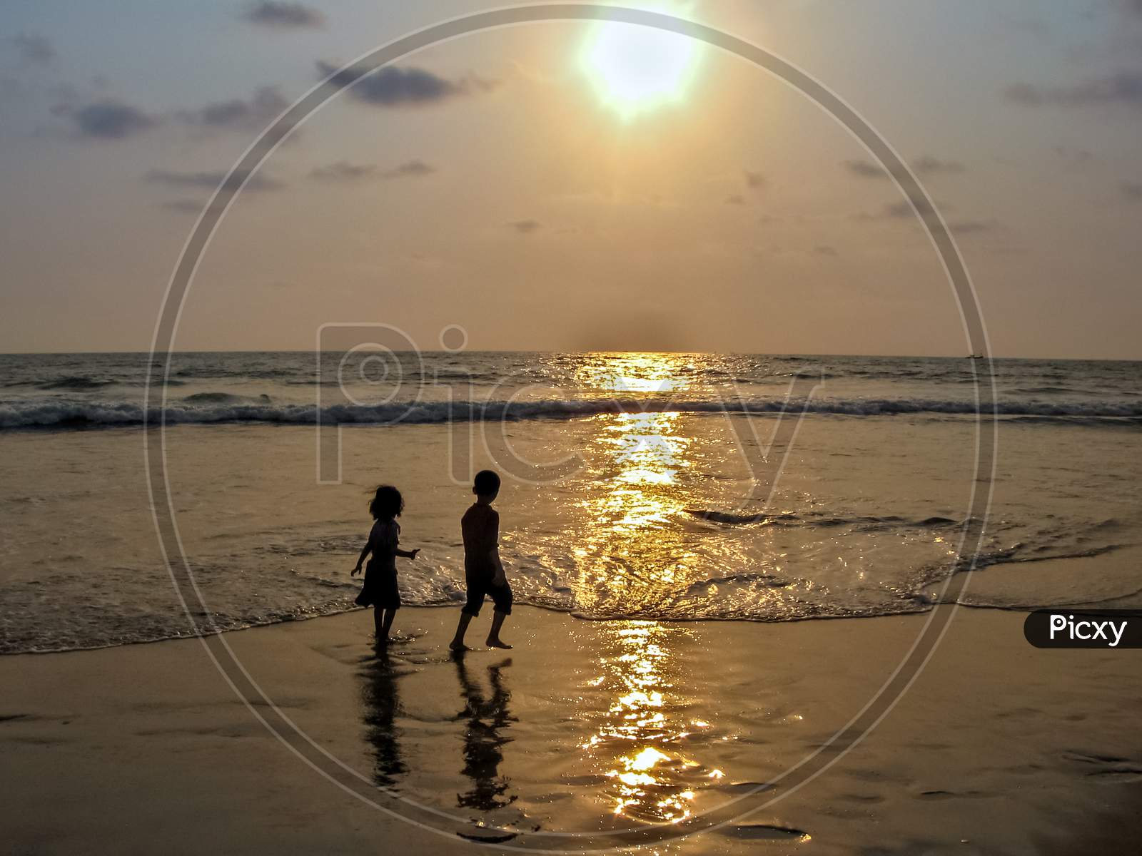 Silhouette Image Of Boy And Girl Playing In Sea On A Background Of Nice Sunset.