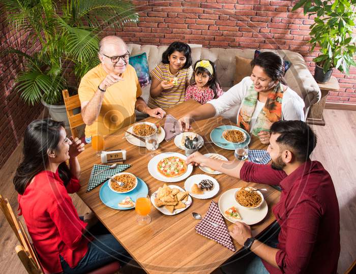 Indian multigenerational Family eating food at dining table at home or restaurant.