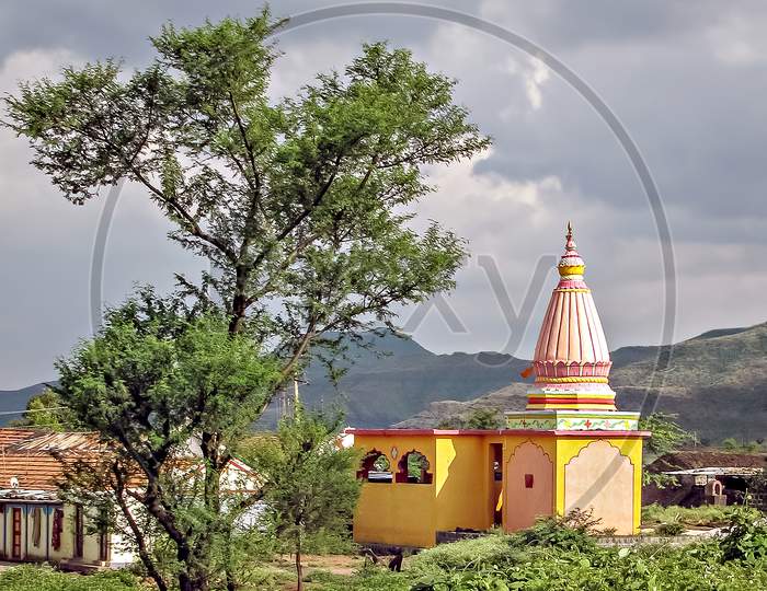 Colorful dome of a small temple with ancient stone wall compound and landscape in village Ambale, Maharashtra, India.