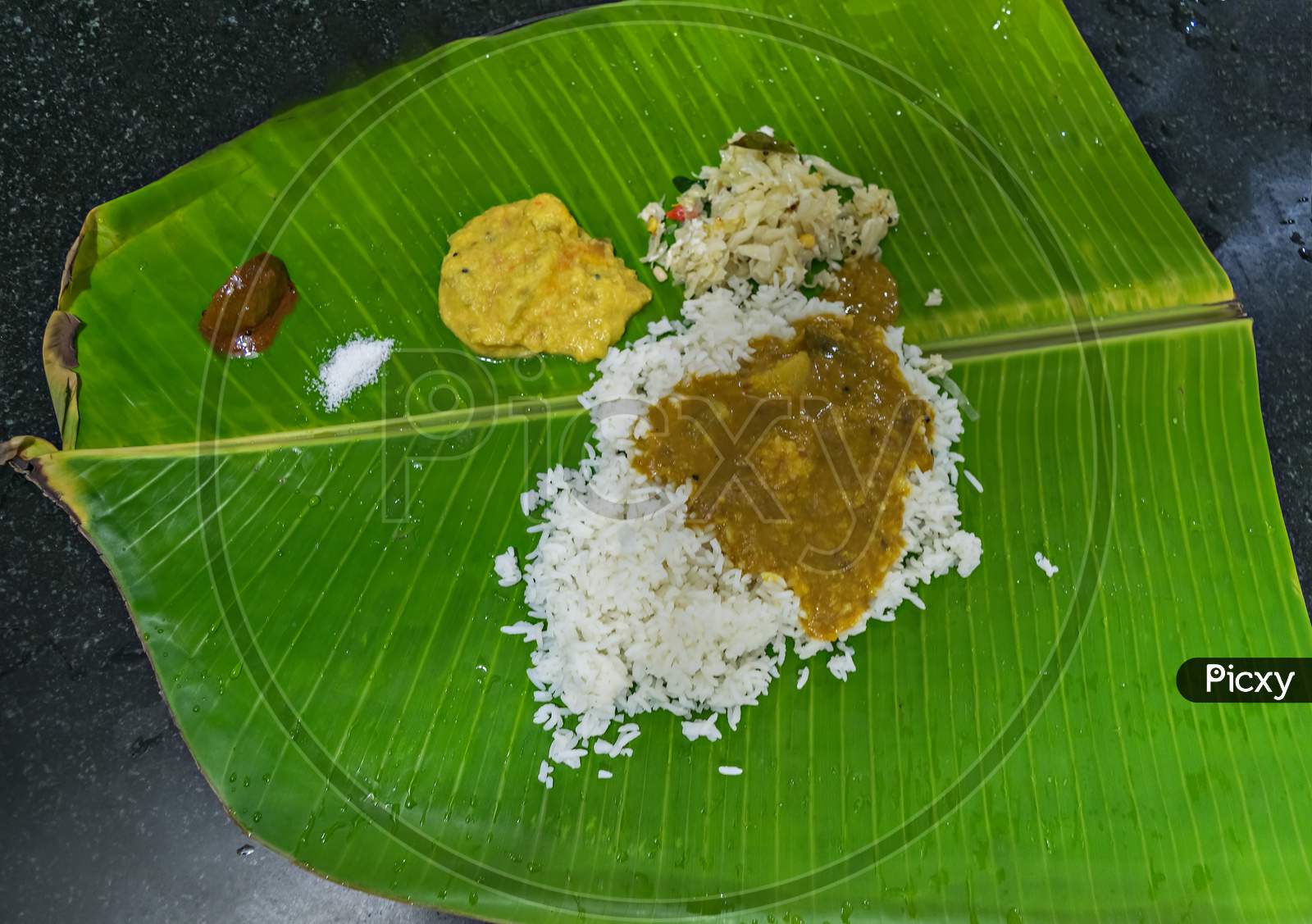 Traditional South Indian Meals Served On Banana Leaf With Rice, Curry, Pickle.