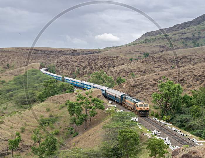 Train Coming Out Of A Hill Cutting With Background Of Mountains And Clouds.