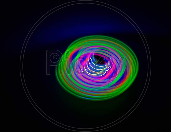 Long Exposure, Slow Shutter, Multicolor Led Light Painting Of A Spinning Top On Abstract Dark Black Background.
