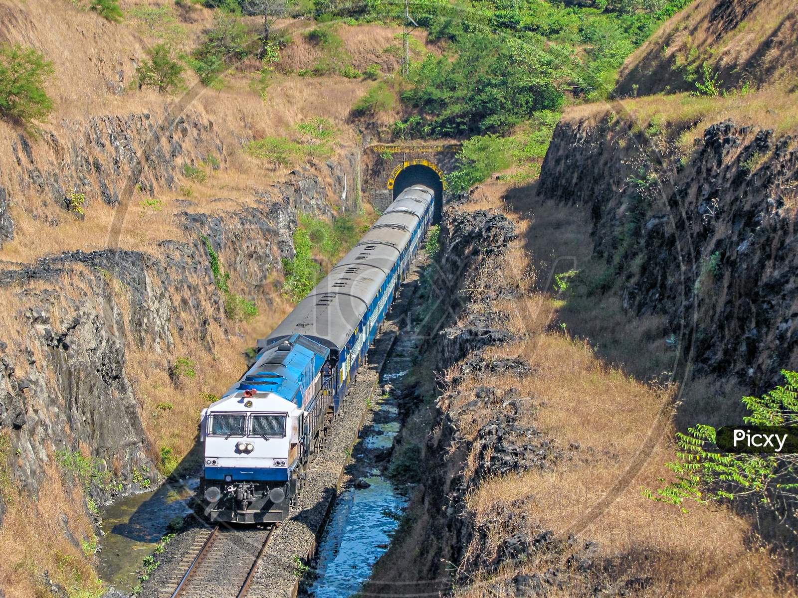 A Passenger Train Coming Out Of A Tunnel Into Deep Cutting In Maharashtra, India.