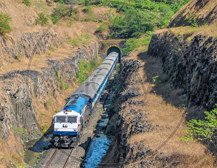 A Passenger Train Coming Out Of A Tunnel Into Deep Cutting In Maharashtra, India.