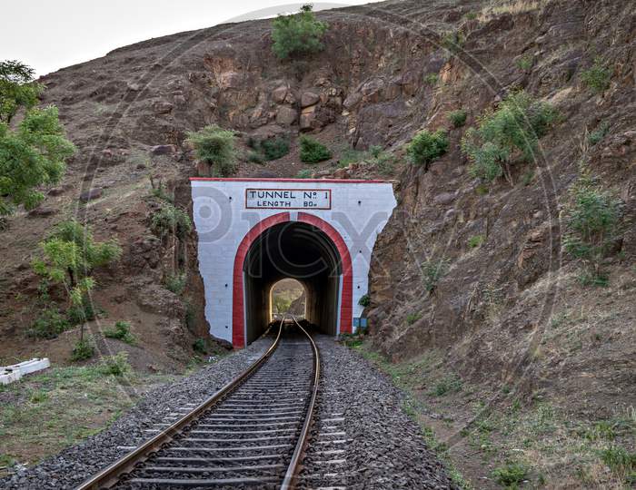 Photo Of A Railway Track Passing Through A Tunnel Cut Through A Rocky Hill.