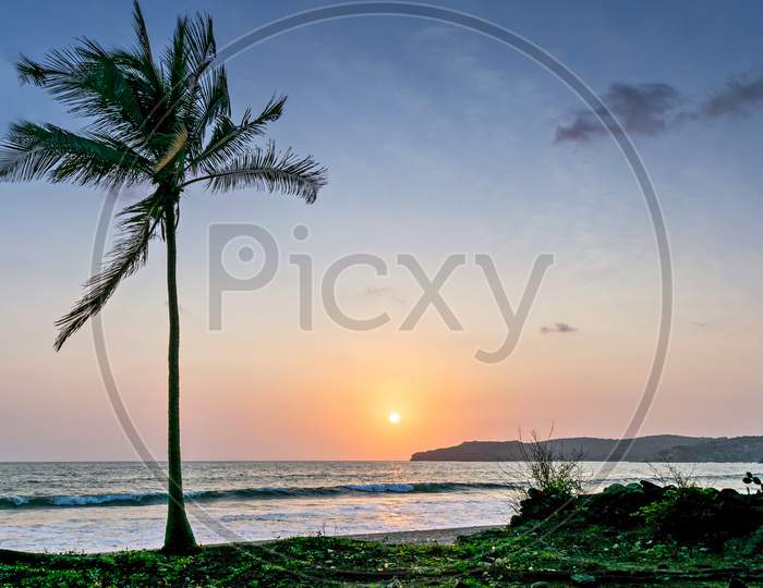 Sun Setting In The Sea With A Coconut Tree On The Shore. Can Be Used As Background.