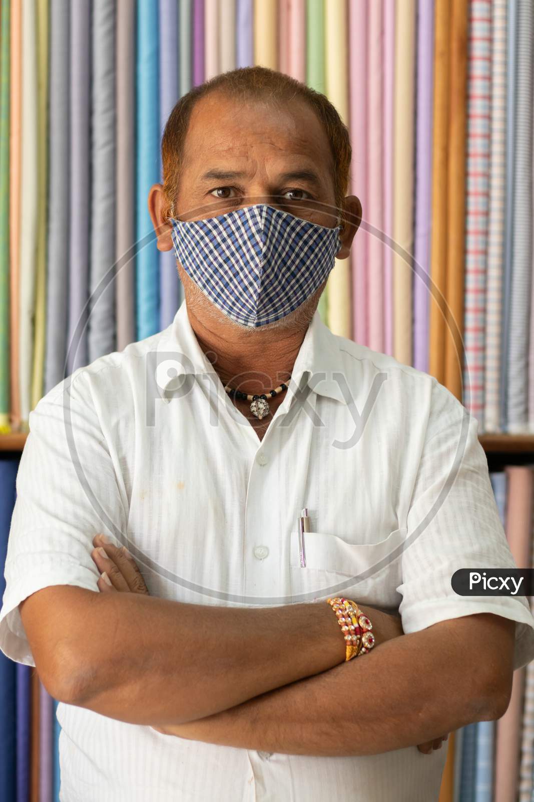 Portrait Of Shopkeeper Looking At Camera In Cloth Store Wearing Protective Medical Mask To Prevent Coronavirus Or Covid-19 And Standing With Arms Crossed