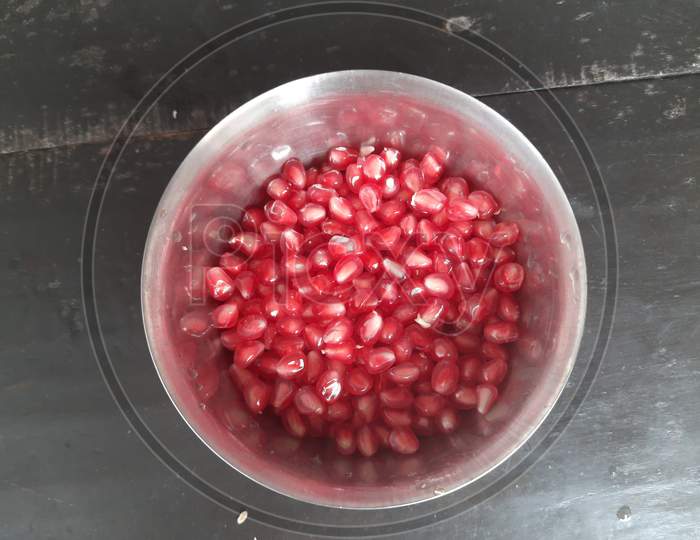Pomegranate seeds in the bowl on black background.