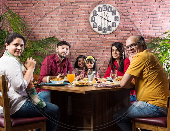 Indian multigenerational Family eating food at dining table at home or restaurant.