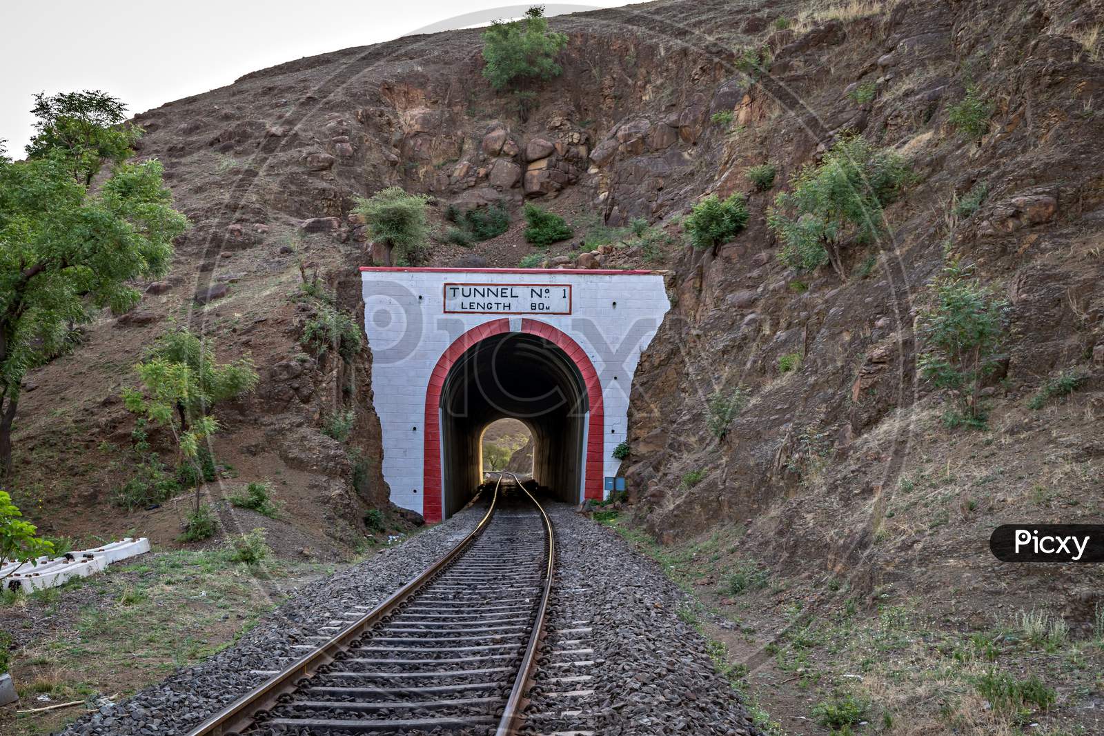 Photo Of A Railway Track Passing Through A Tunnel Cut Through A Rocky Hill.