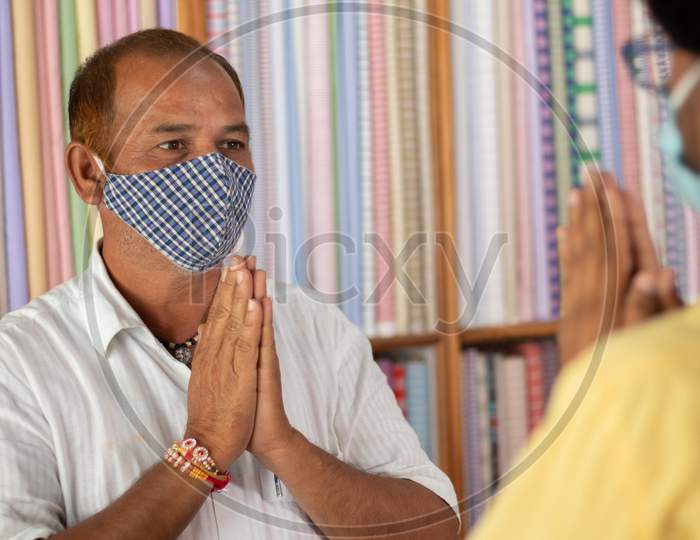 Shopkeeper Greeting Customer With Namaste Hand Gesture And Wearing Medical Mask To Stop And Spreading Of Coronavirus Or Covid-19 Pandemic At Workplace Or Shops - Concept Of New Normal And Business Lifestyle.