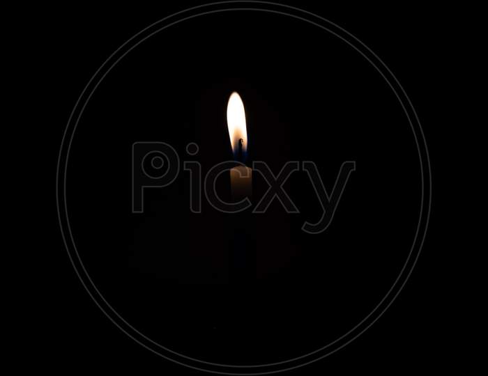 Close Up Single Burning, Bright White Paraffin Candle Light On Isolated Dark Black Background. Red, orange, yellow candle fire flame smoke in party festival celebration at night. Copy Space For Text.