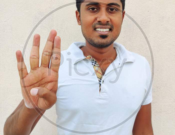 Smiling South Indian Young Man Wearing White Tshirt Pointing Up With Fingers Number Four. Isolated On White Background.