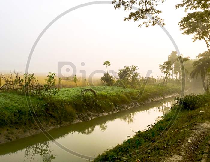 A Canal Flowing Beside A Grassy Field