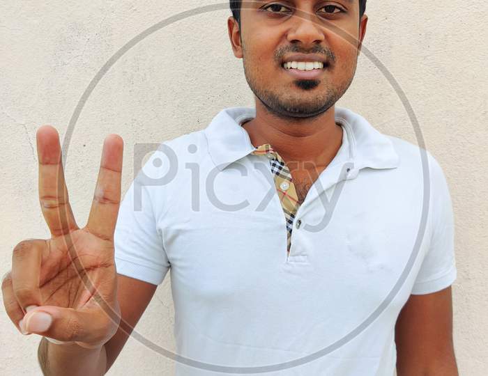 Smiling South Indian Young Man Wearing White Tshirt Pointing Up With Fingers Number Two. Isolated On White Background.