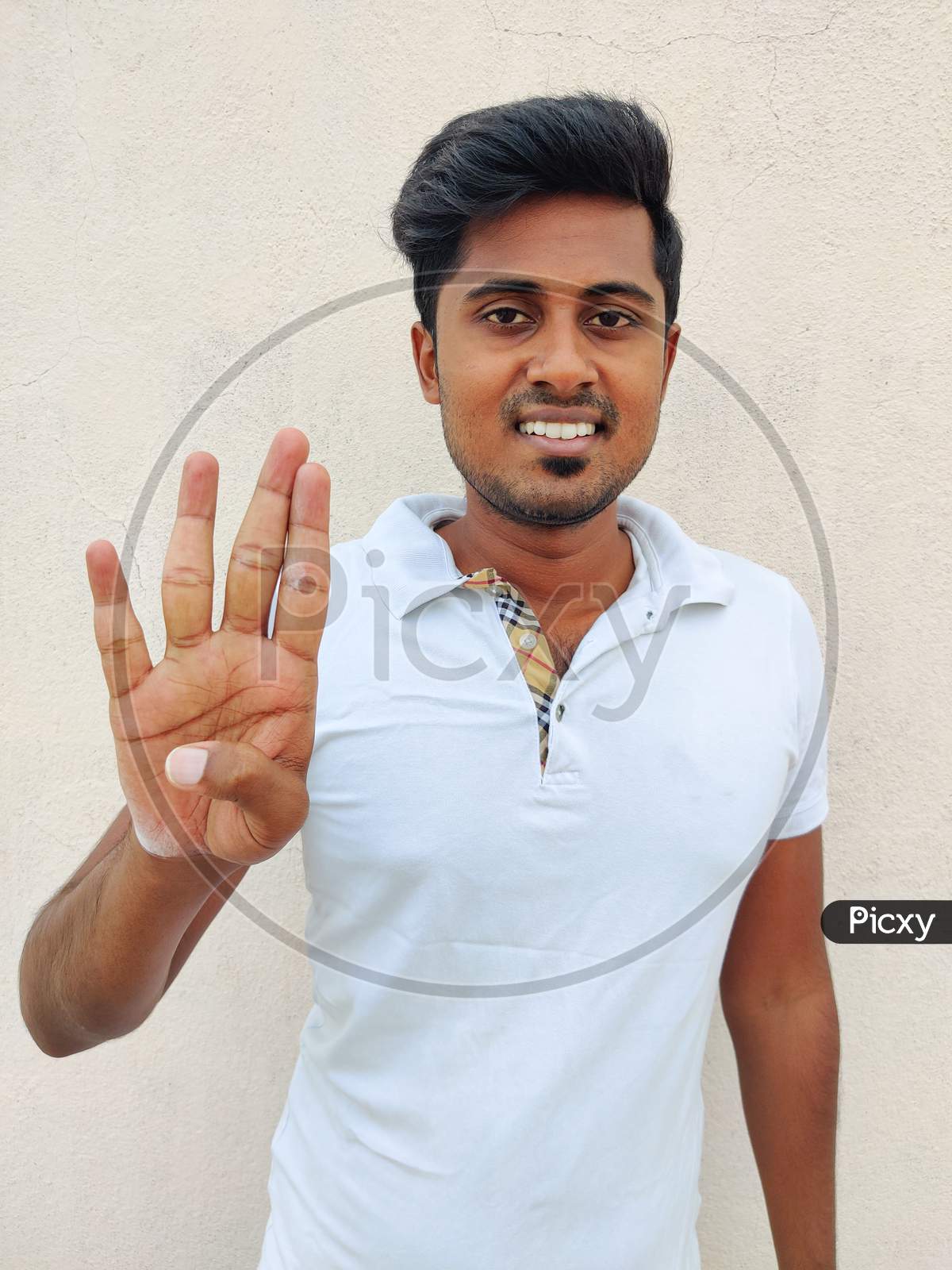 Smiling South Indian Young Man Wearing White Tshirt Pointing Up With Fingers Number Four. Isolated On White Background.