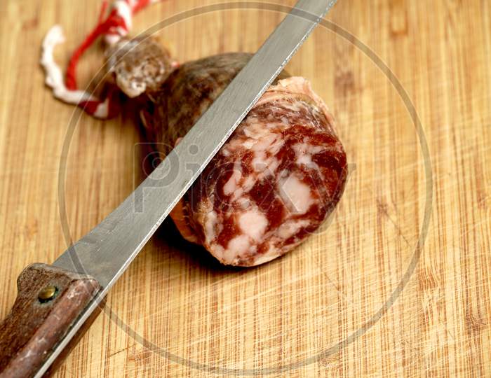 Close Up View Of Spanish Sausage Called Salchichon Or Chorizo On A Bamboo Wood Board With A Knife. Spanish Food