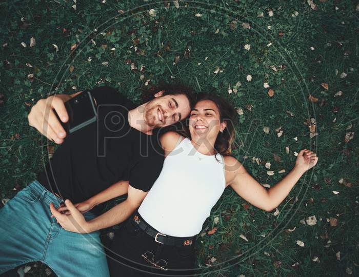 Young Couple Taking A Selfie While Lying On The Grass