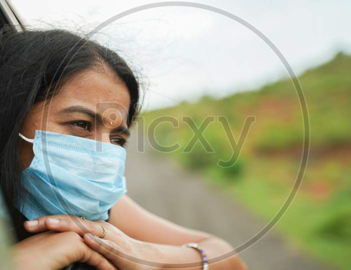 Sad Young Girl In Medical Mask To Protect From Coronavirus, Covid-19 Or Pollution And Watching Out From Moving Car Window - Concept Of Travel, Vacation And Road Trip.