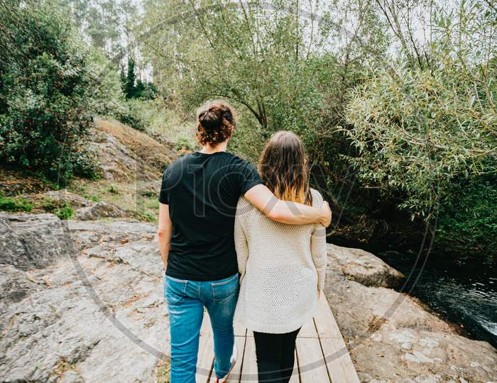 Back View Shot Of A Young Couple Taking A Walk Near The River Over A Wooden Path