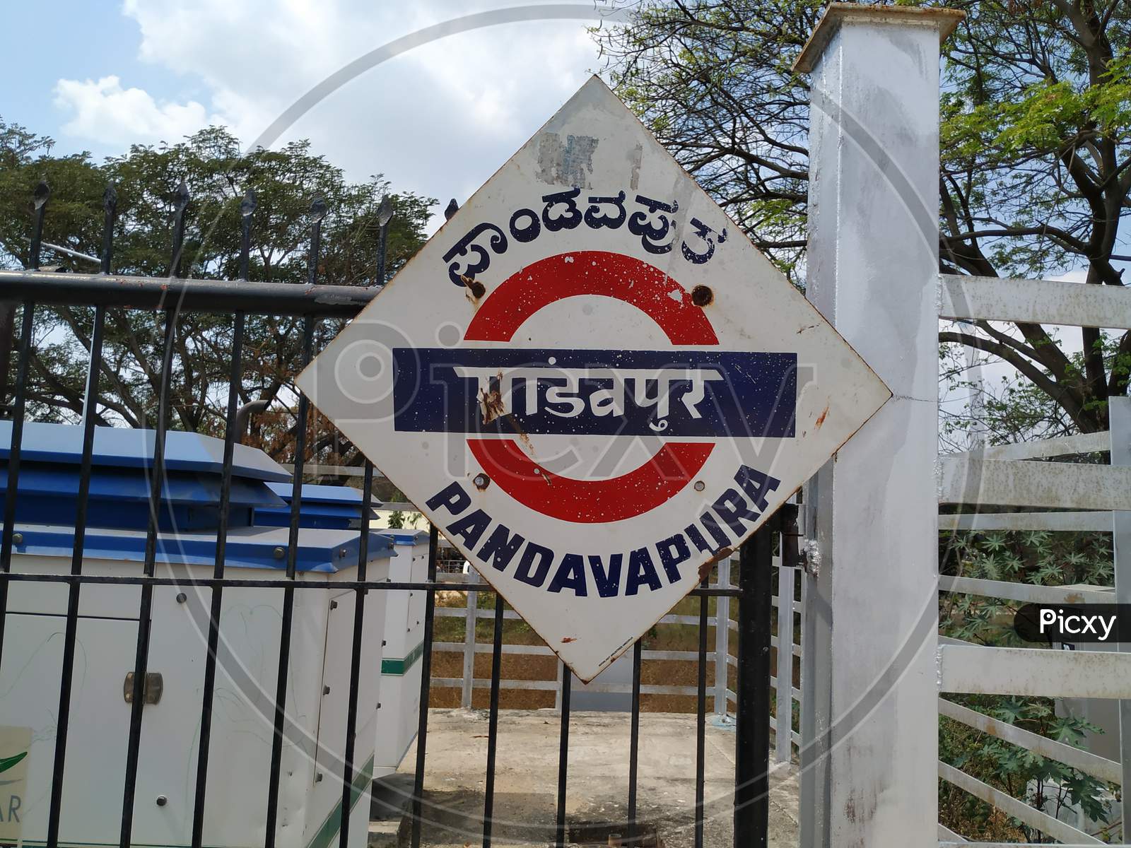 Location Name Board Of Pandavapura, In A Railway Station In A Diamond Shape With Red And Blue Color.