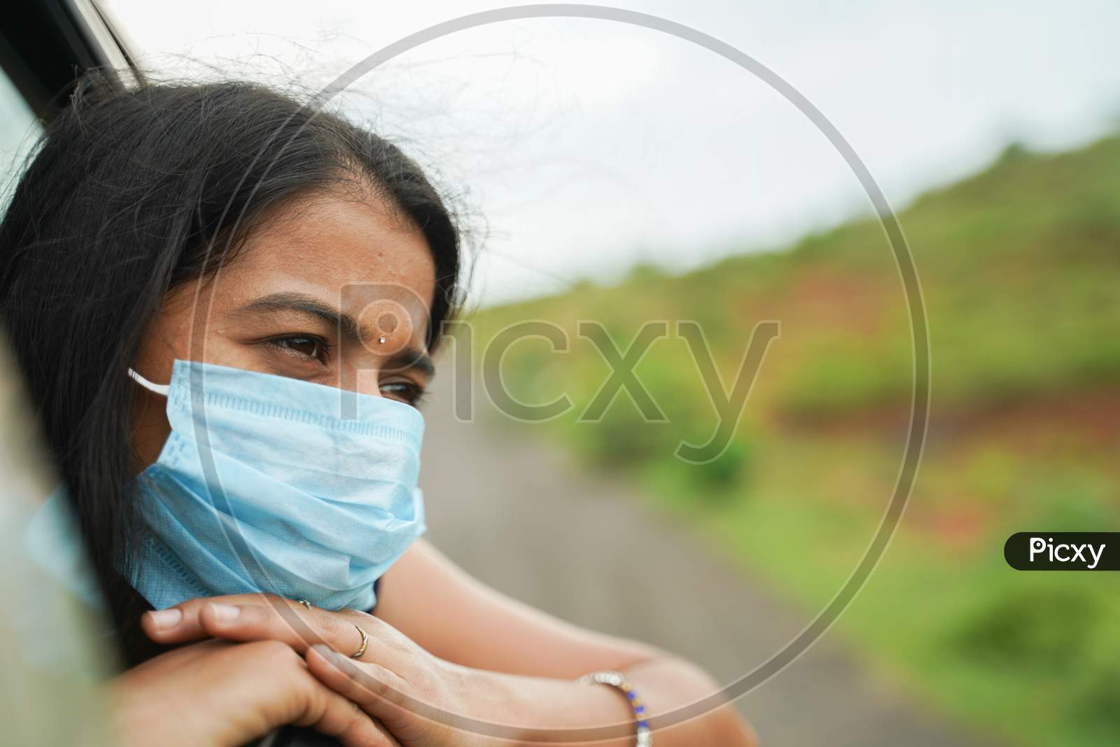 Sad Young Girl In Medical Mask To Protect From Coronavirus, Covid-19 Or Pollution And Watching Out From Moving Car Window - Concept Of Travel, Vacation And Road Trip.