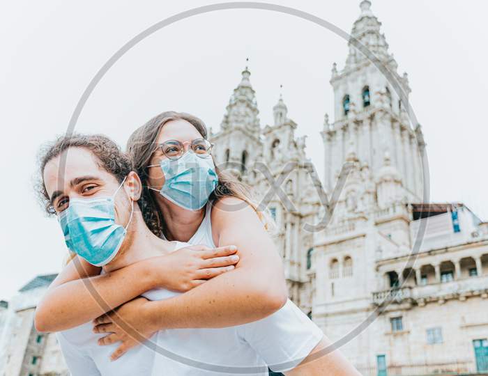 Young And Happy Couple With The Masks Put On In Front Of An Ancient Cathedral While Traveling