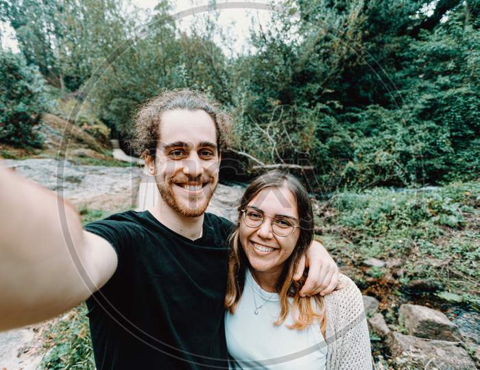 Selfie Of A Young Couple Giving A Bis Smile To The Camera On The Forest