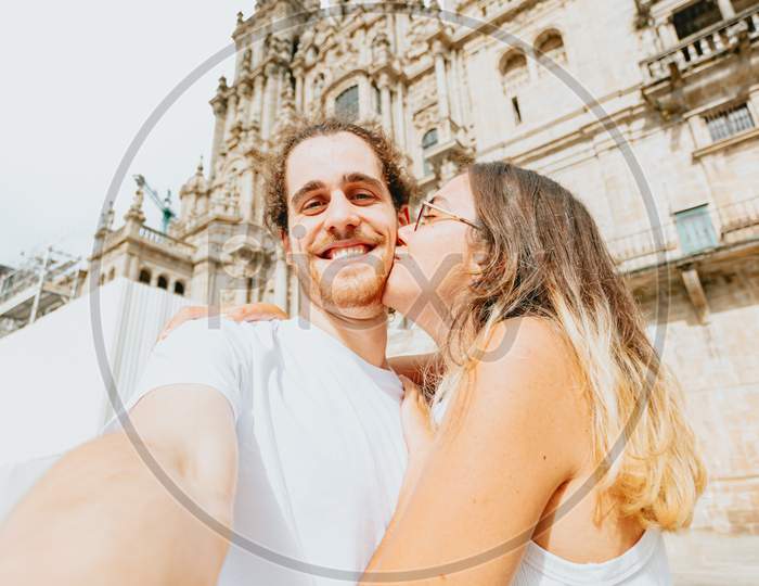 Young Couple Kissing In Front Of A Cathedral During A Sunny Day