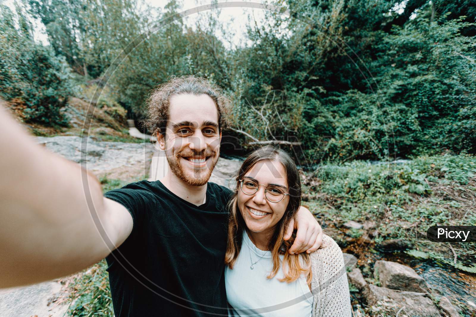 Selfie Of A Young Couple Giving A Bis Smile To The Camera On The Forest