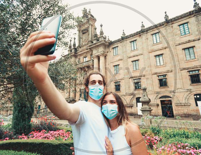Young Couple Taking A Fancy Selfie With The Masks On In A Garden In Front Of An Old Building