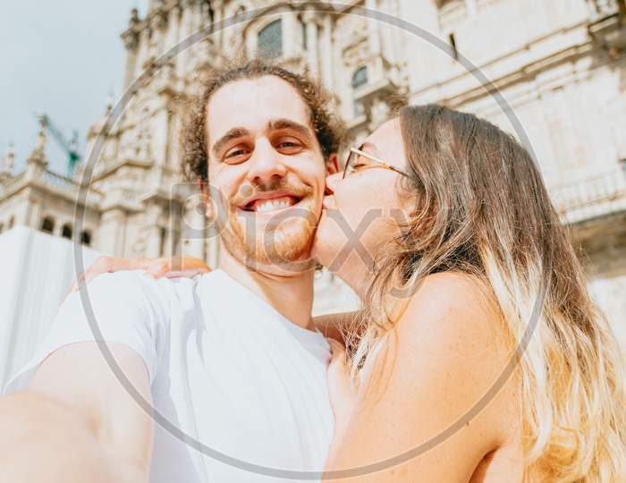 Young Couple Kissing In Front Of A Cathedral During A Sunny Day