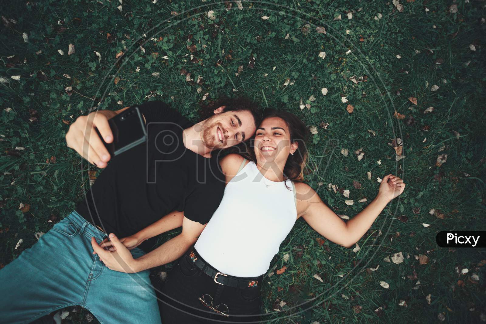 Young Couple Taking A Selfie While Lying On The Grass
