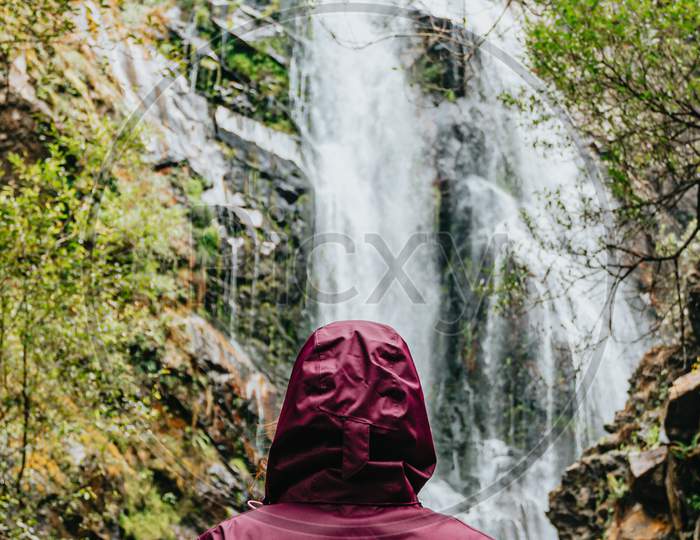 Woman In A Purple Oilskin Standing In Front Of A Giant Waterfall