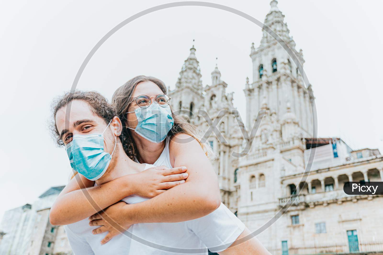 Young And Happy Couple With The Masks Put On In Front Of An Ancient Cathedral While Traveling