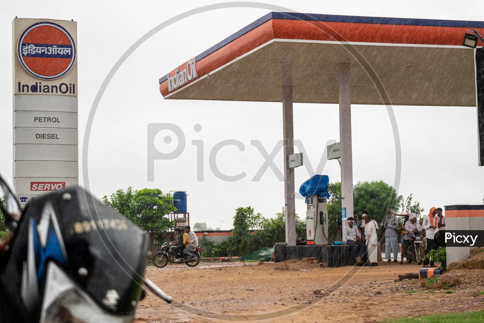 people standing under a shade to avoid rain at Indian oil petrol pump