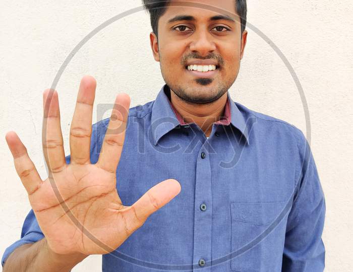 Smiling South Indian Young Man Wearing Blue Shirt Pointing Up With Fingers Number Five. Isolated On White Background.