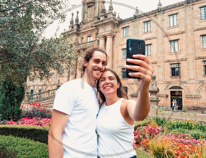 Young Couple Taking A Fancy Selfie In A Garden In Front Of An Old Building